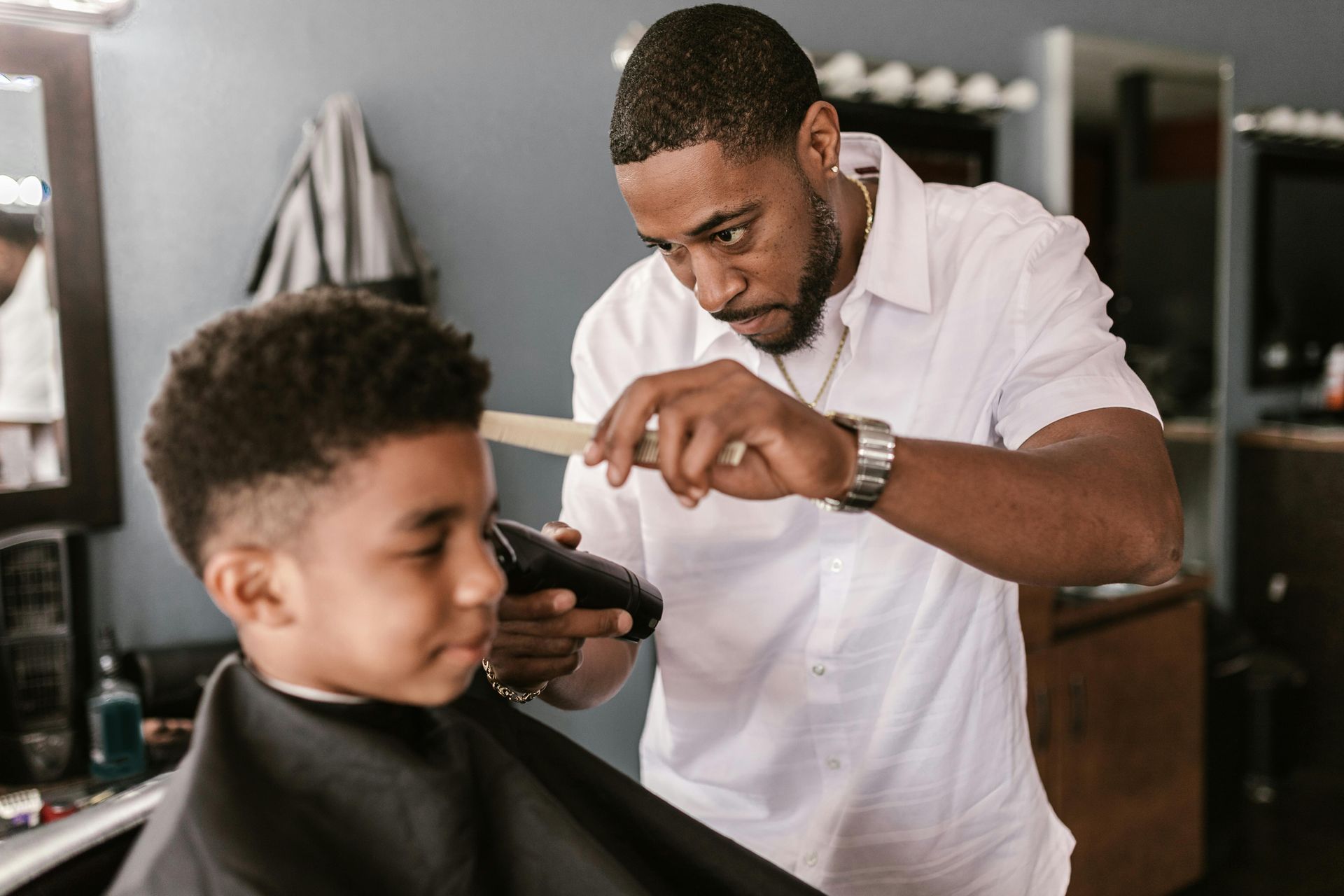 Barber giving a young boy a haircut with clippers in a barbershop.