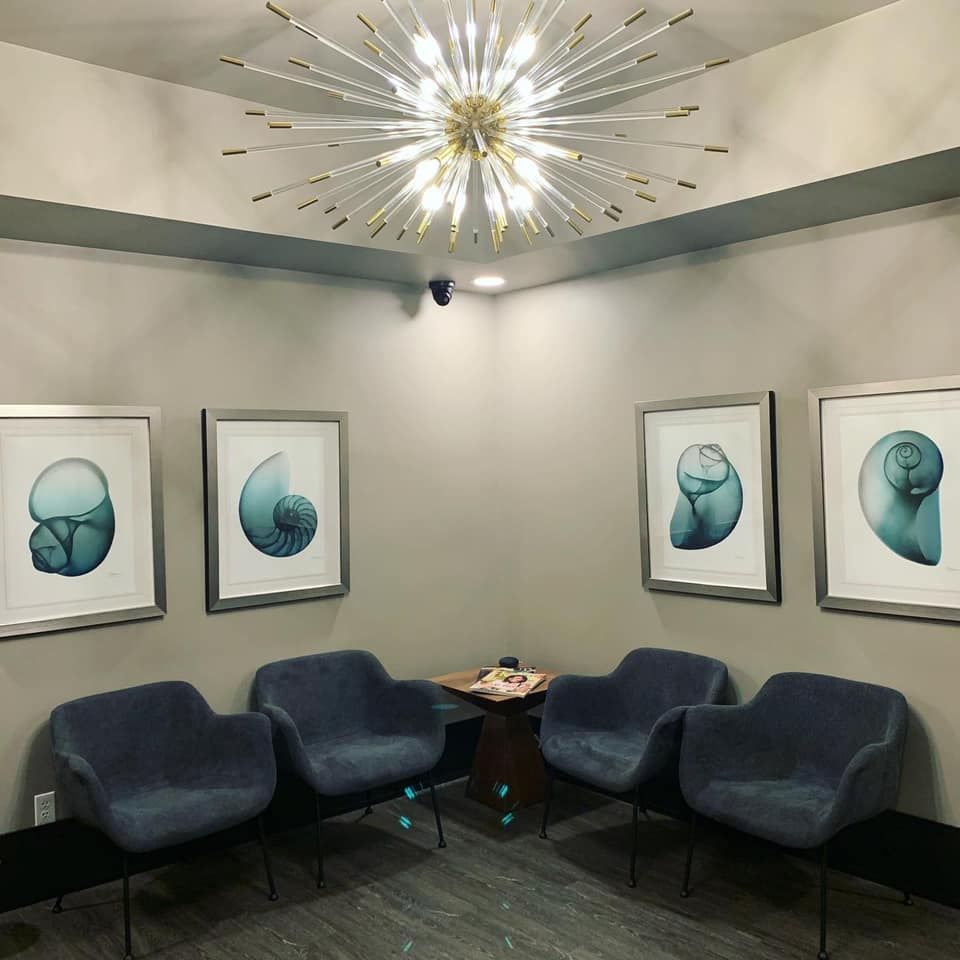 A modern waiting room with four blue chairs, seashell art, and a sputnik chandelier.