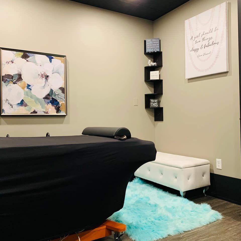 Massage room with a black-covered table, light green walls, and a blue rug.
