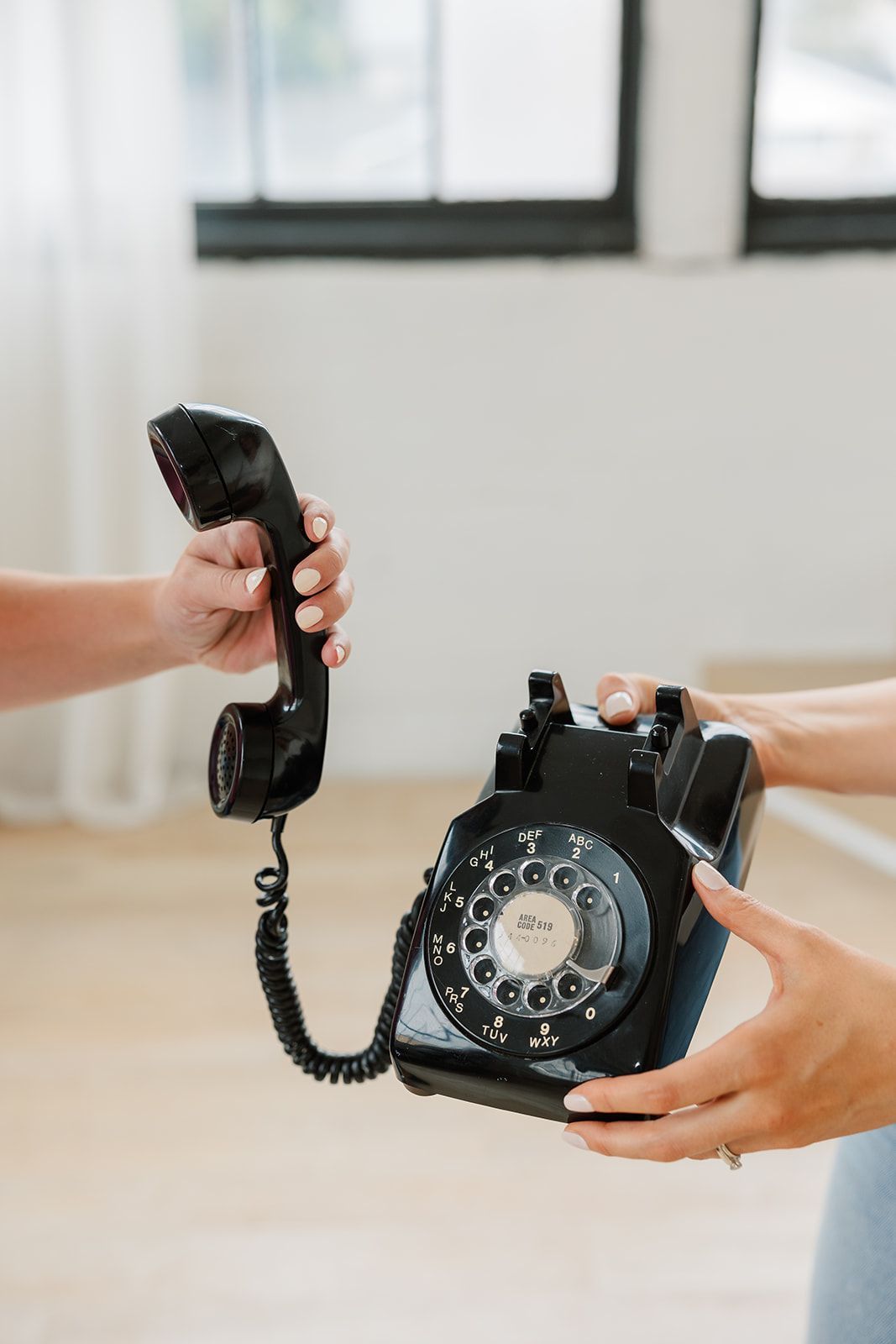 Two people are holding a black telephone in their hands.
