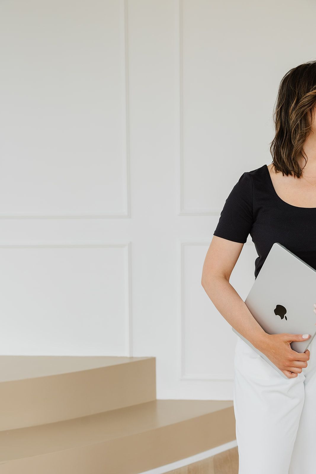 A woman in a black shirt and white pants is holding an apple laptop.