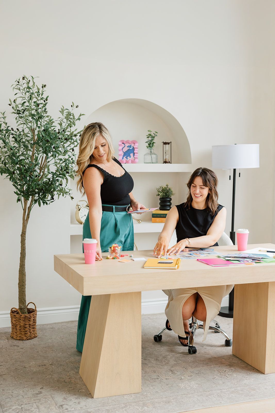 Two women are standing next to each other at a desk in an office.