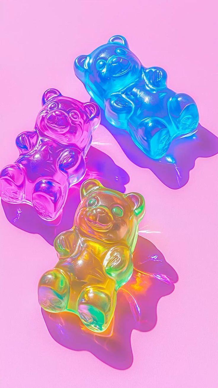 Three translucent gummy bear candies: purple, blue, and yellow on a pink background.