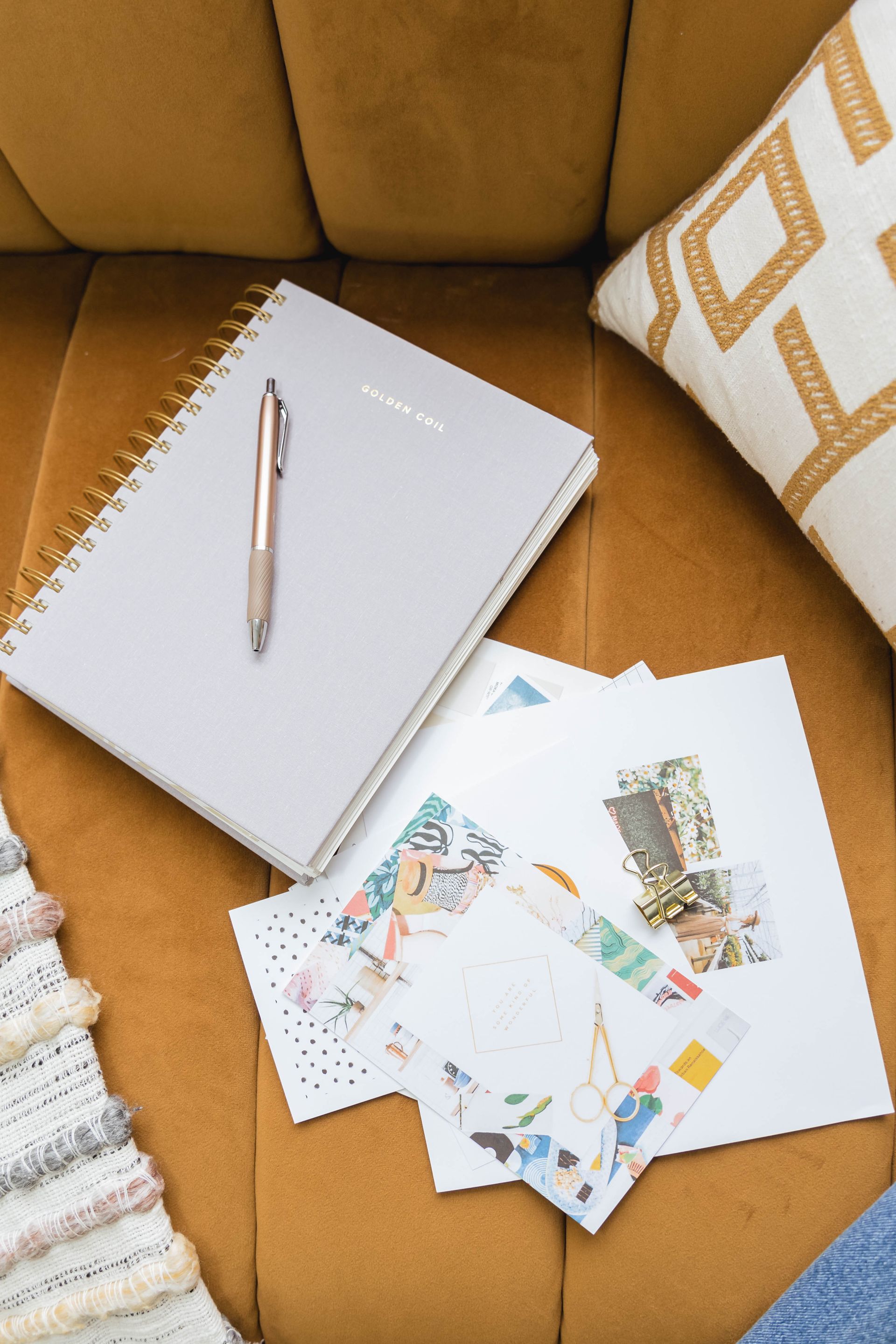 A person is sitting on a couch with a notebook , pen , and envelopes.