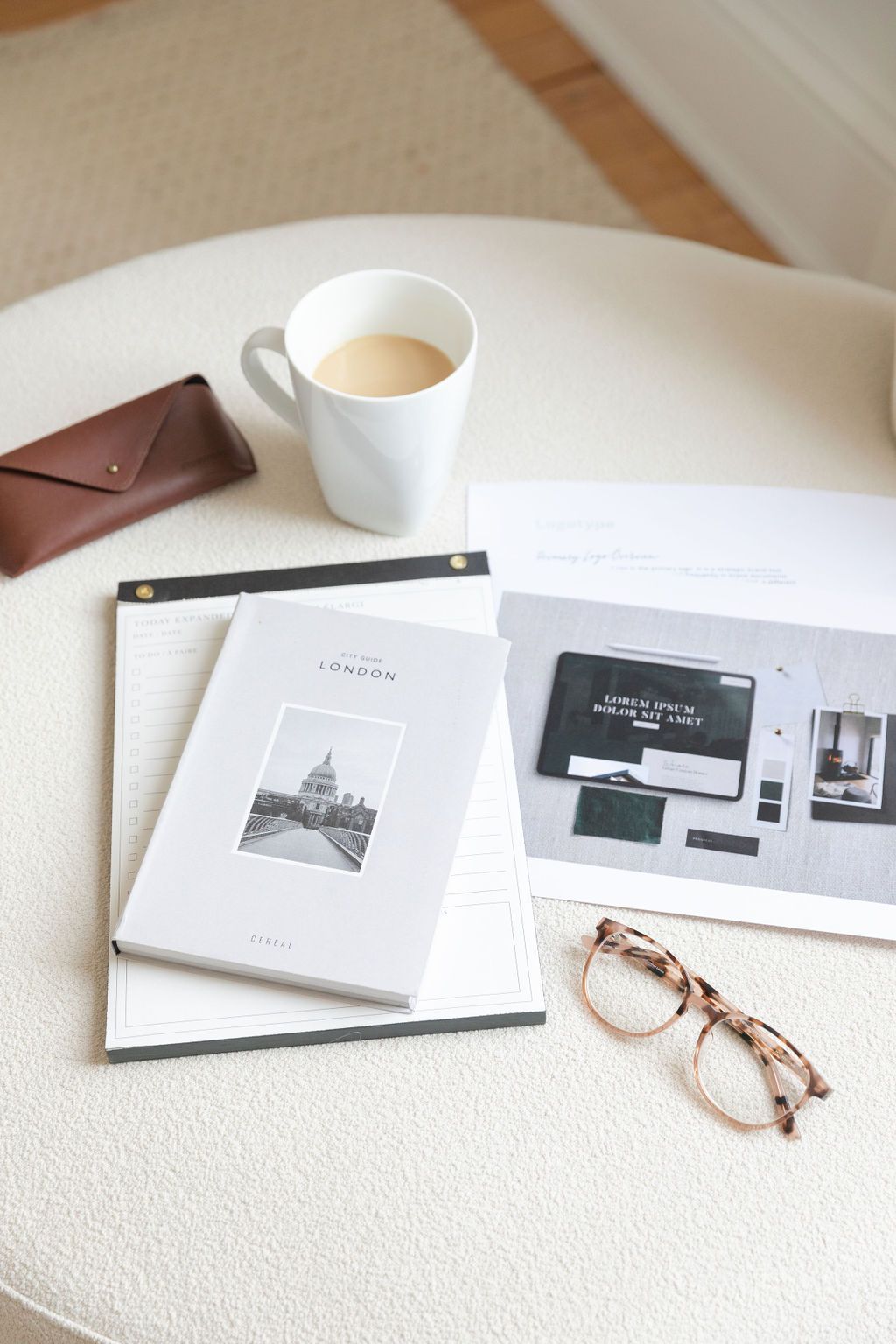 White mug of coffee, glasses, notebook, and documents on an off-white cushioned seat.