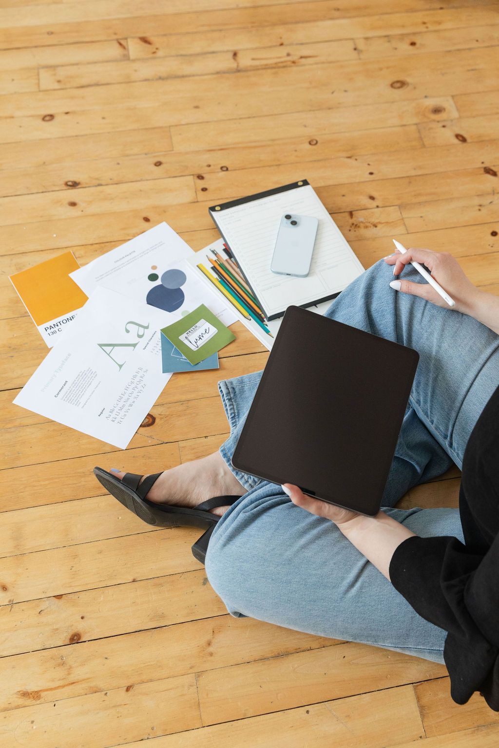Person sitting on wooden floor with tablet, papers, and phone, working.