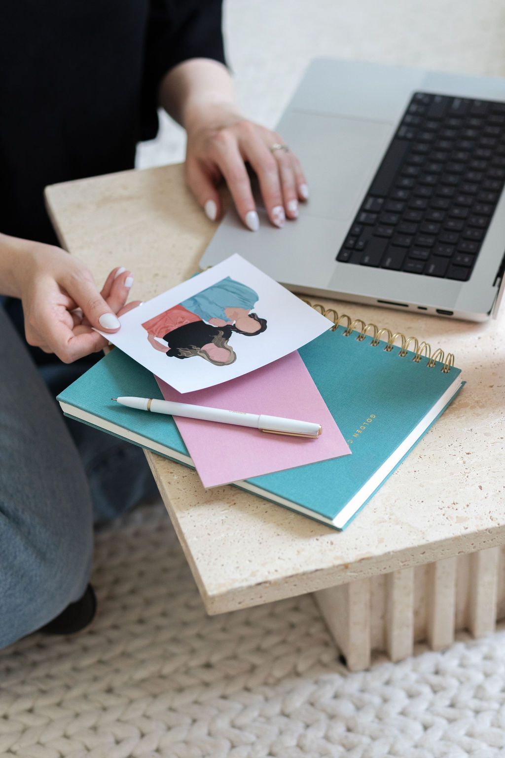 A brand designer is sitting at a table with a laptop and notebooks.