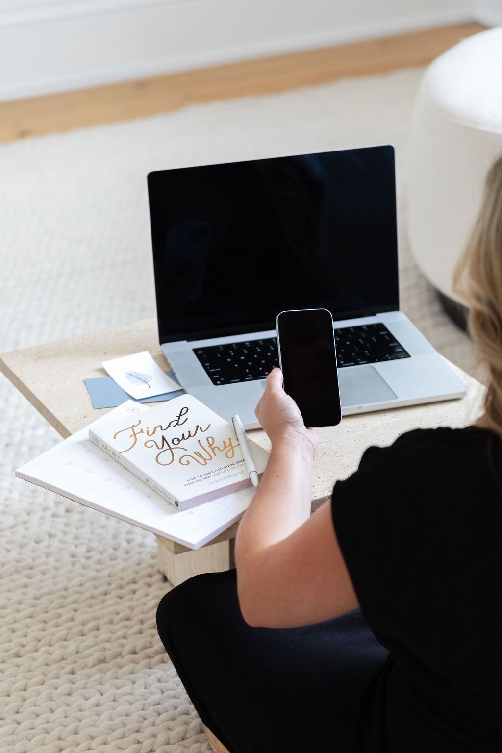 A woman is sitting on the floor using a laptop and a cell phone.
