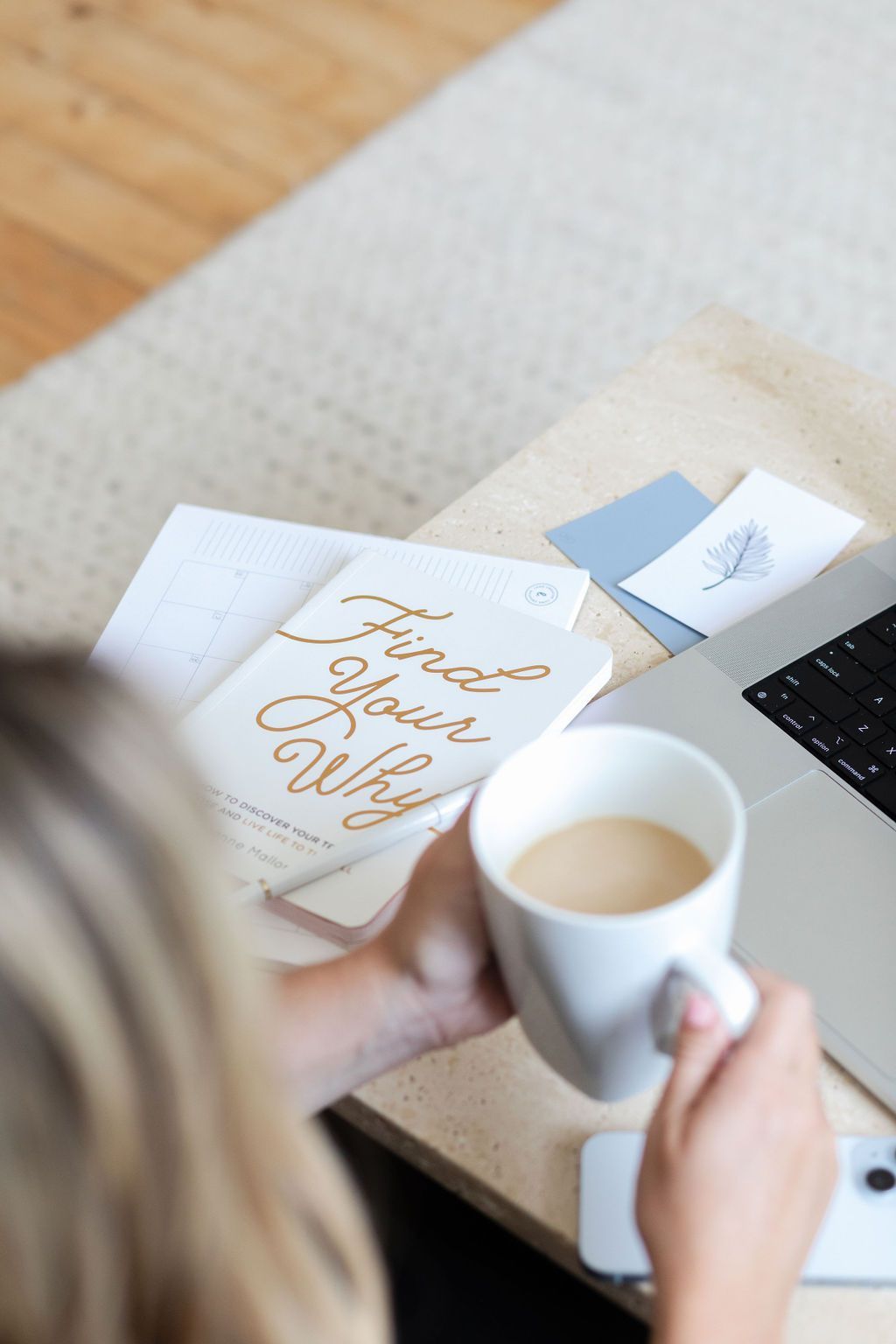 A female brand designer is holding a cup of coffee in front of a laptop & scattered colour swatches