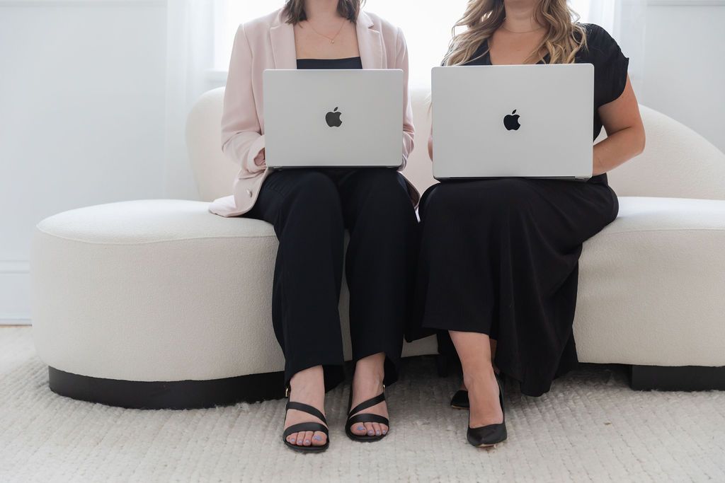 lume team on white sofa, working on MacBooks. One wears a pink blazer, the other a black dress.