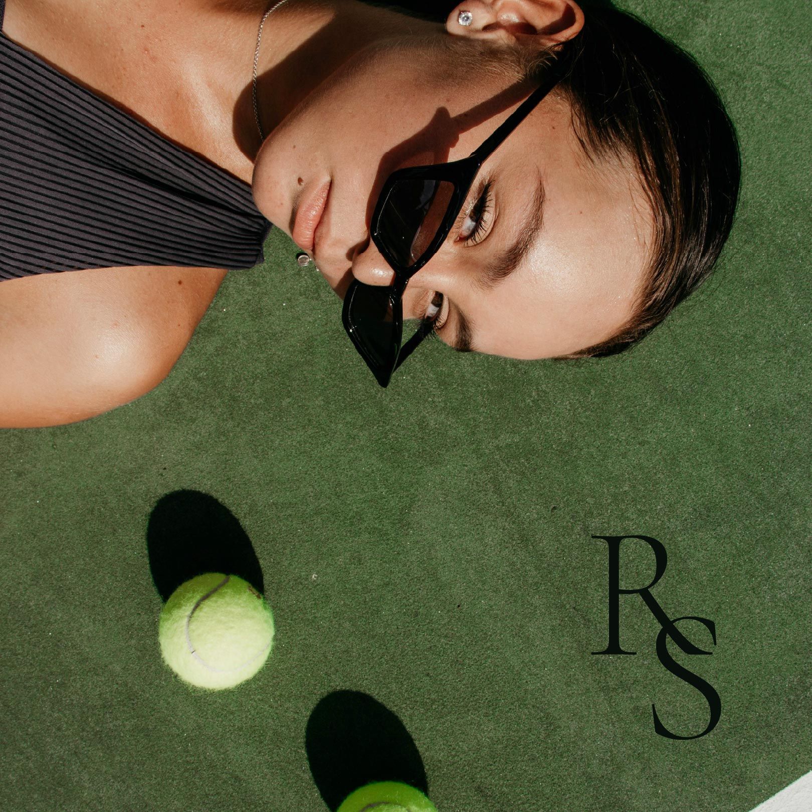 A woman wearing sunglasses is laying on a tennis court
