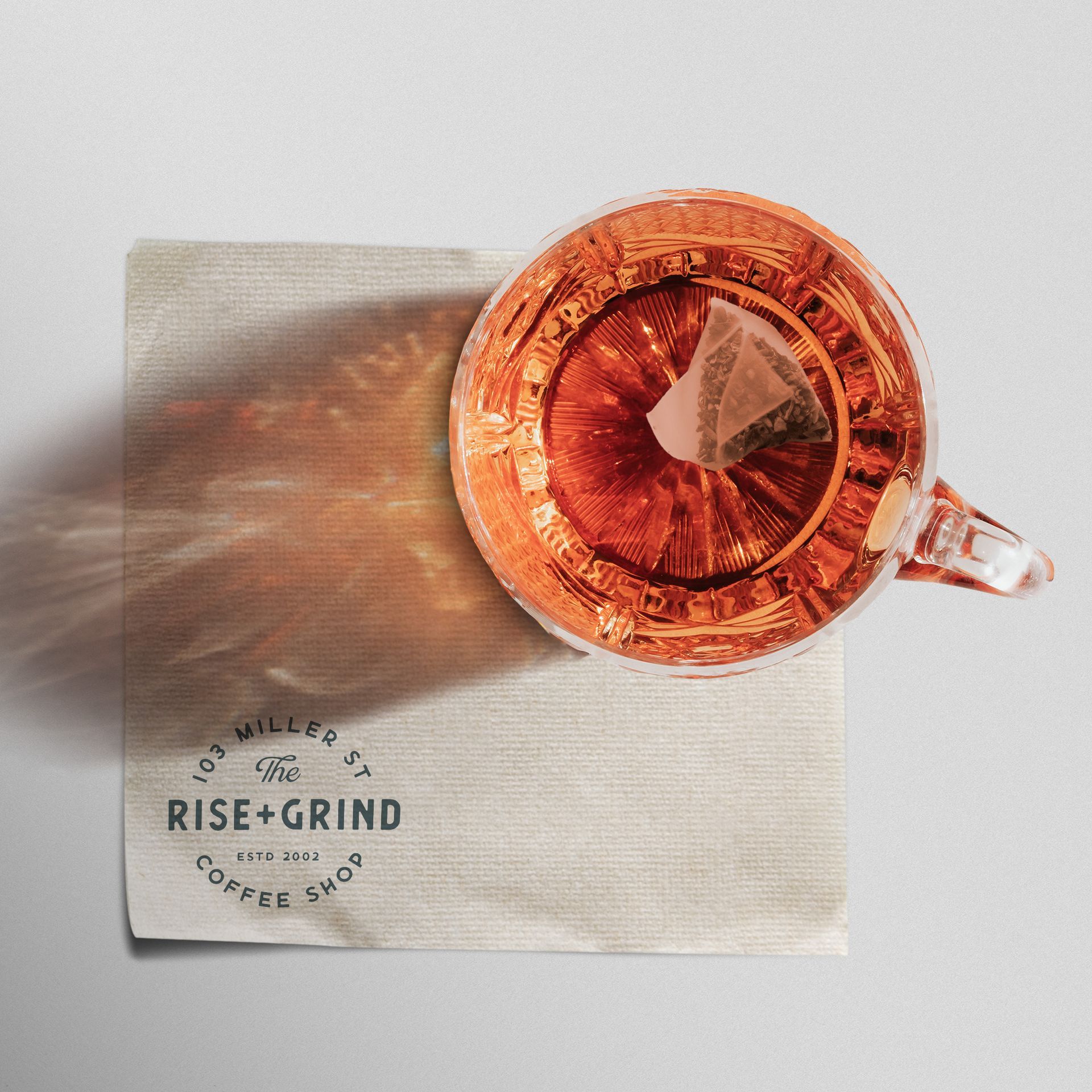 A cup of tea sits on a napkin that says rise grind showing new logo for small business
