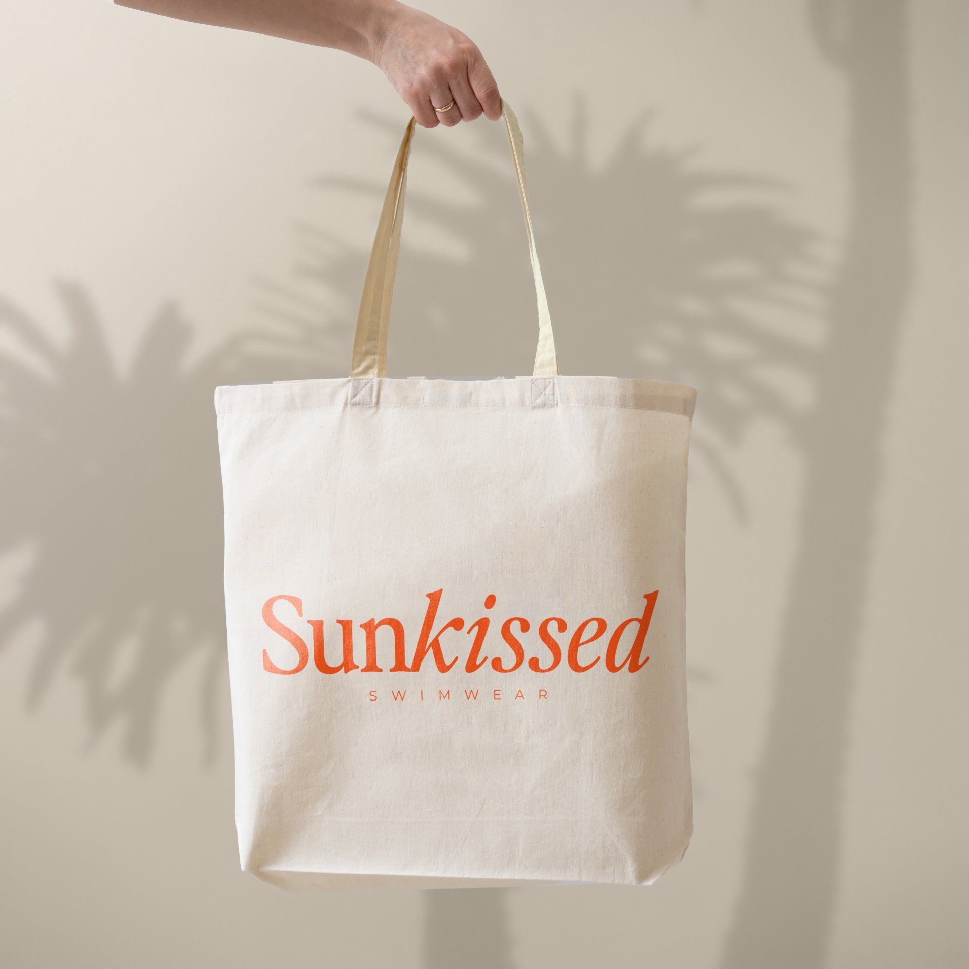 A person is holding a white tote bag that says sunkissed