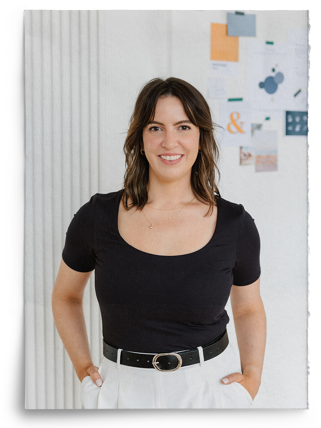 A woman in a black shirt and white pants is standing with her hands in her pockets
