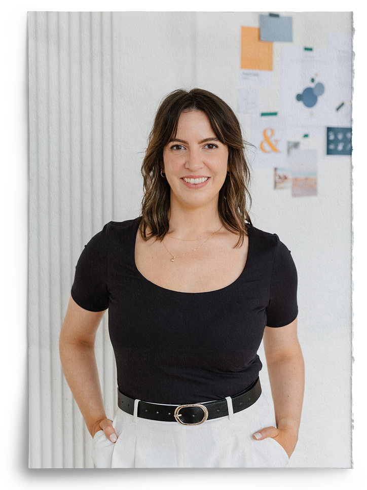 A woman in a black shirt and white pants is standing with her hands in her pockets