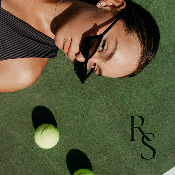 A woman wearing sunglasses is laying on a tennis court