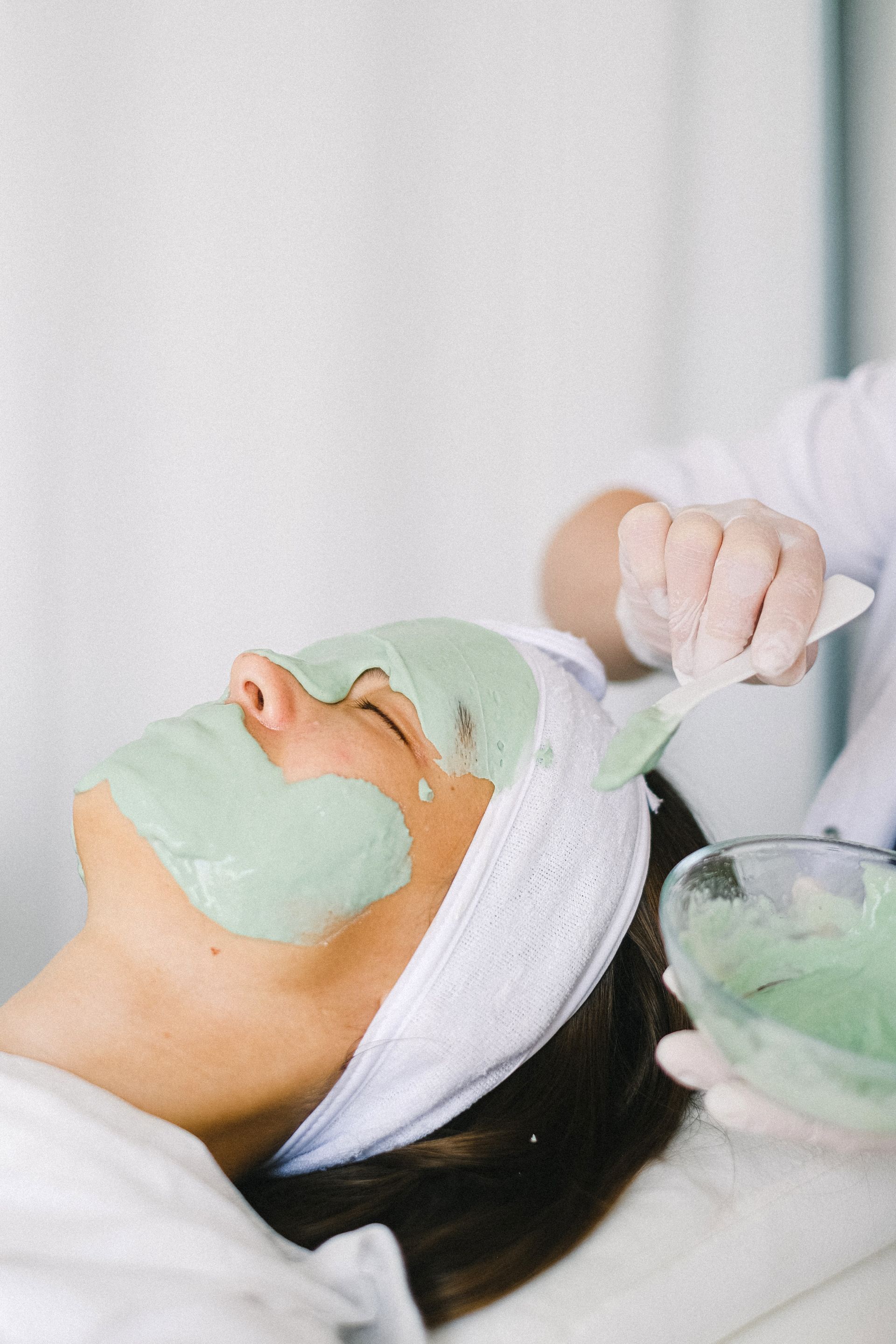 A woman is getting a green mask on her face.
