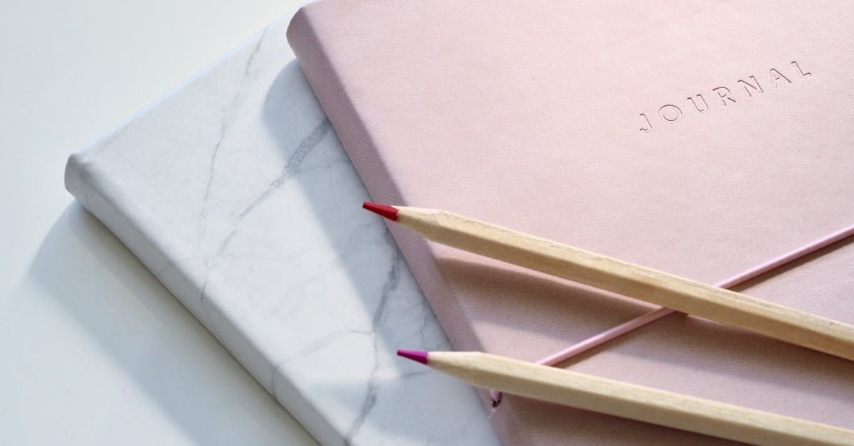 Three pencils are sitting on top of a pink notebook.