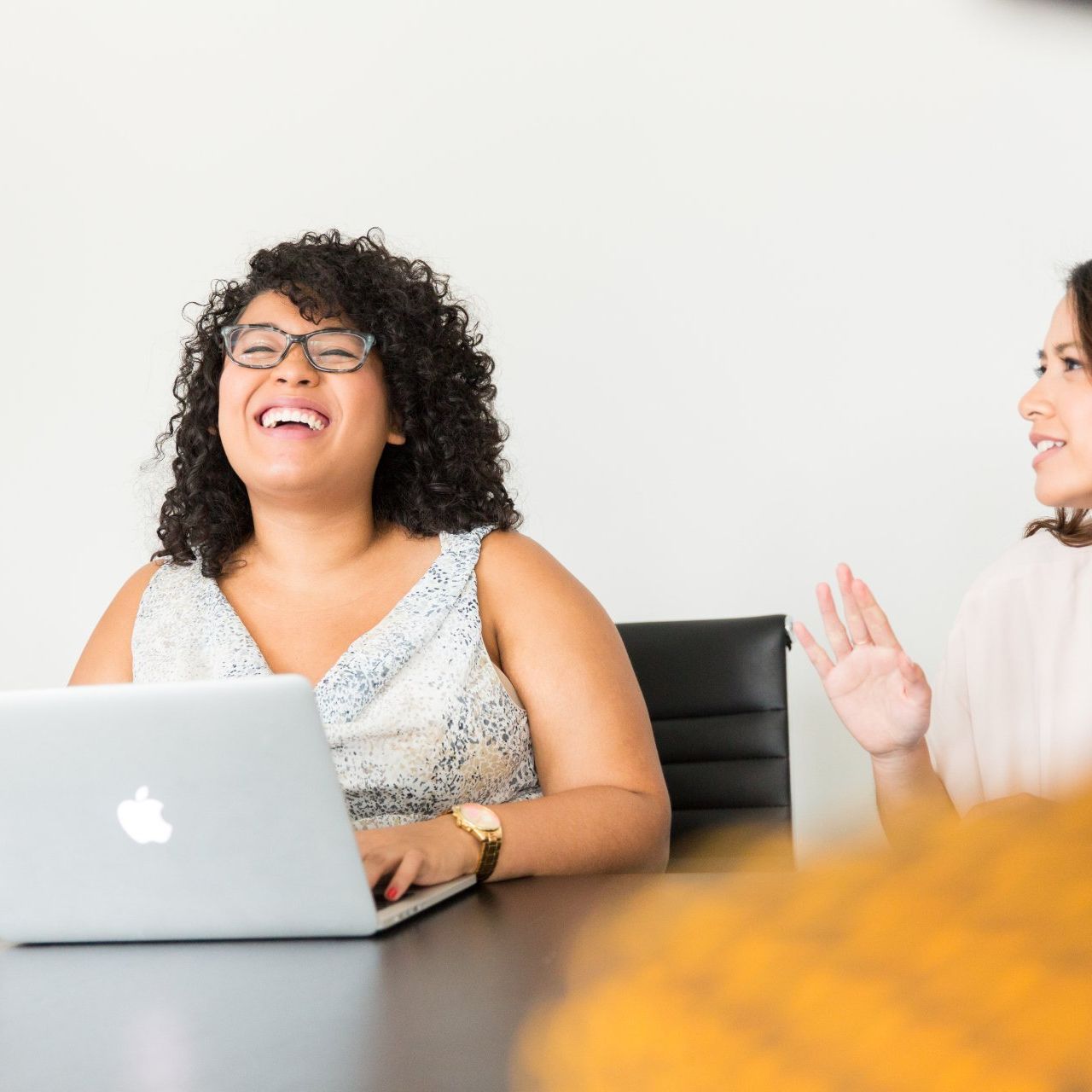 Two women are sitting at a table with an apple laptop