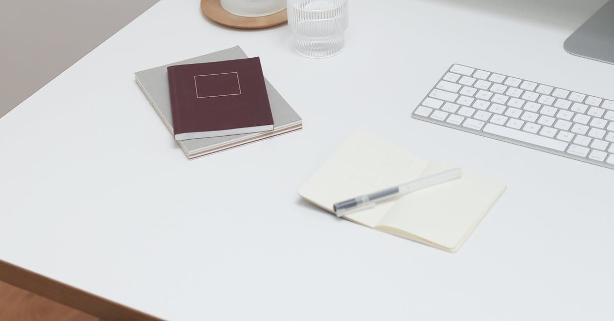 A white desk with a keyboard , notebooks , and a pen.