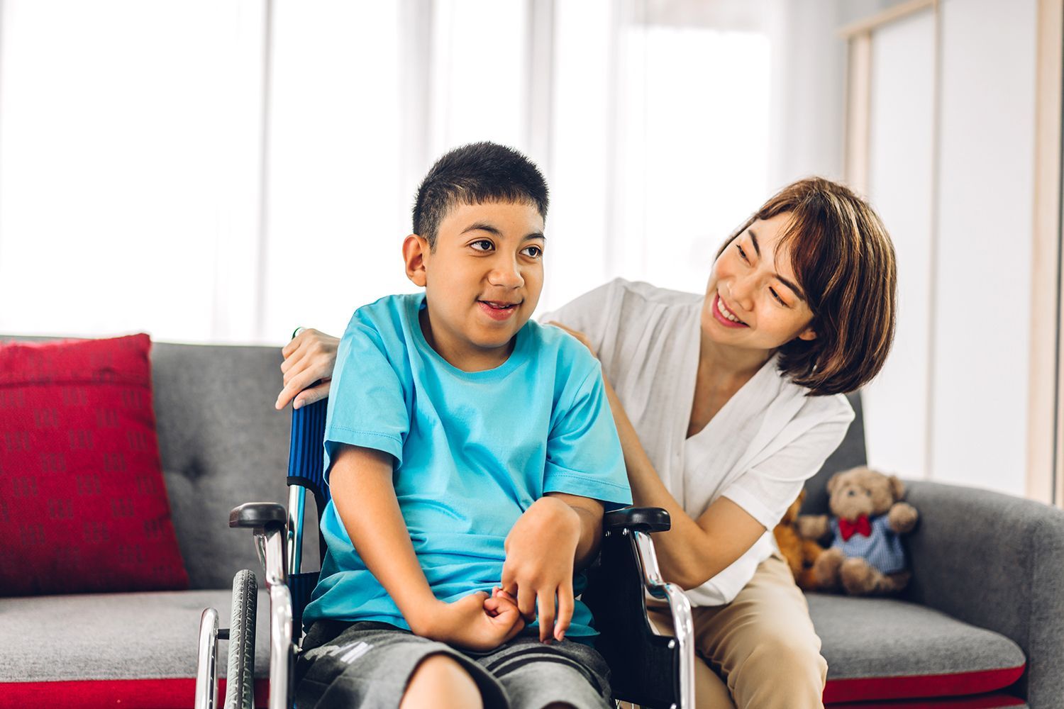 Carer spending quality time with a disabled child seated in a wheelchair at home.