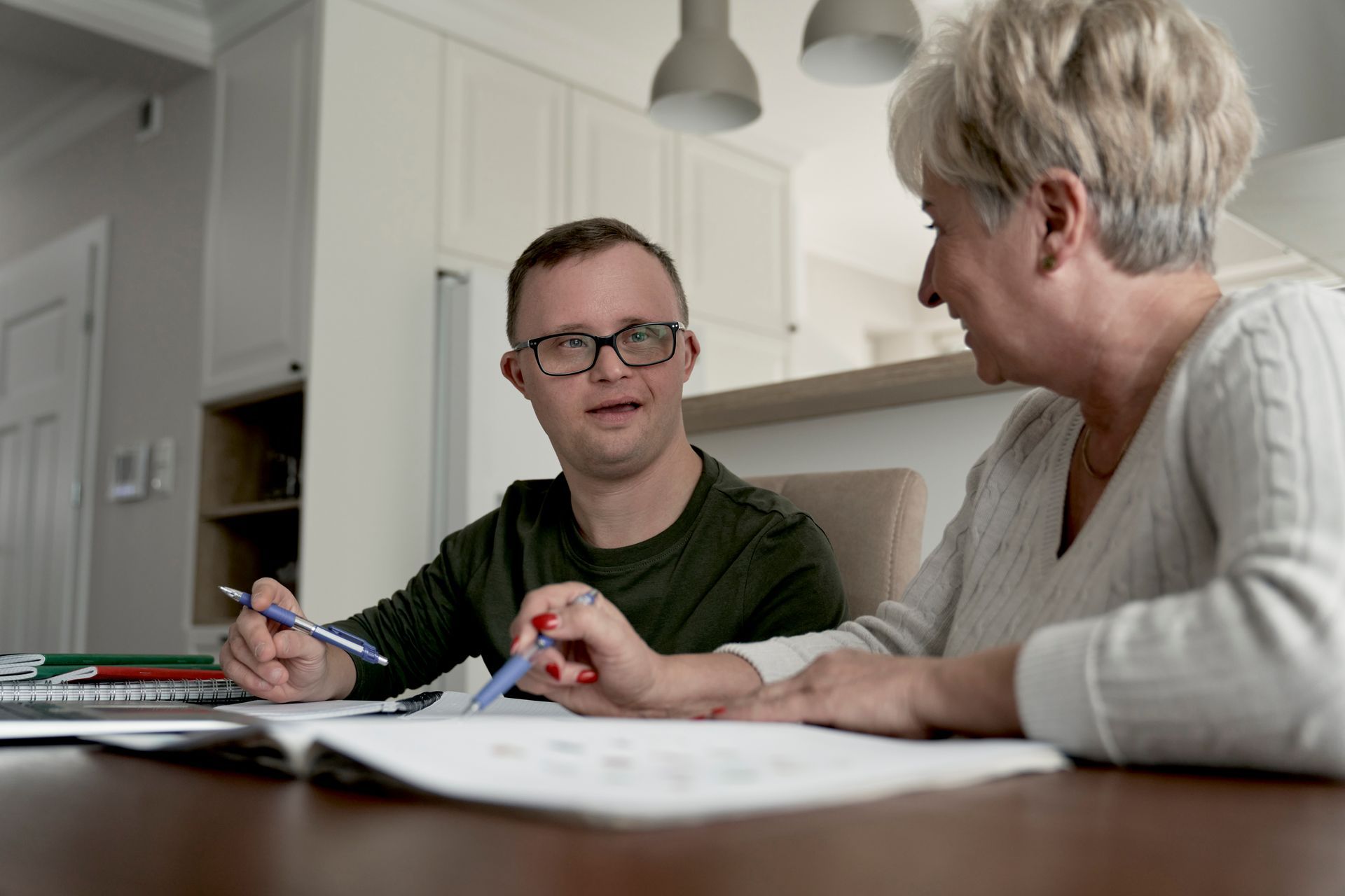 View of a young man with Down syndrome and an elderly woman giving him support inside a house.
