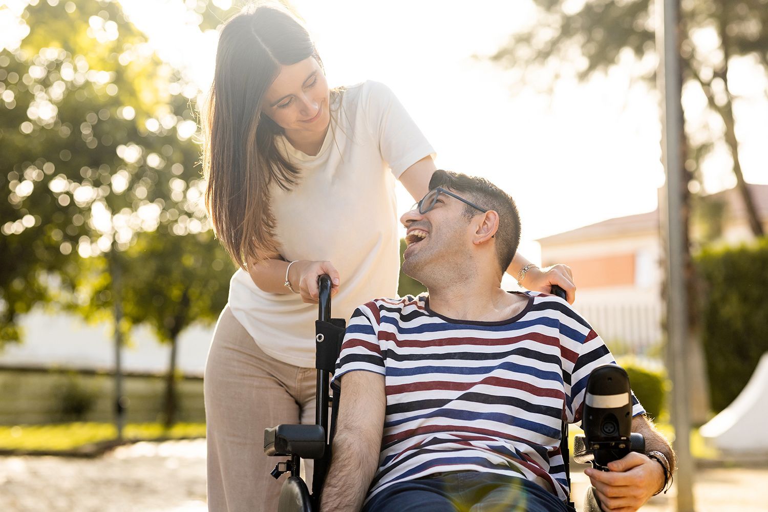 An adult man using a powered wheelchair talking with a young woman in a park.