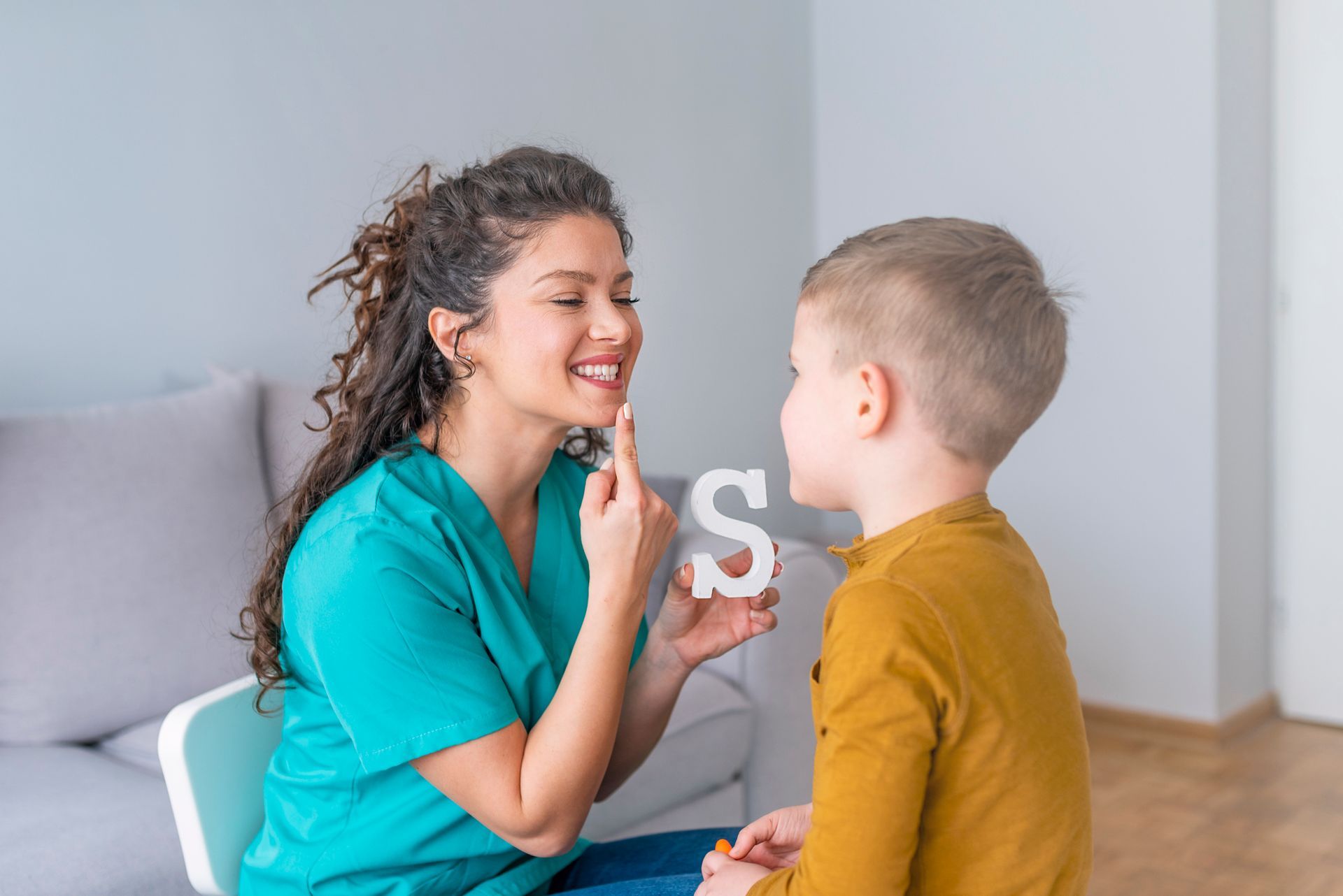 A woman is teaching a young boy how to say the letter s.