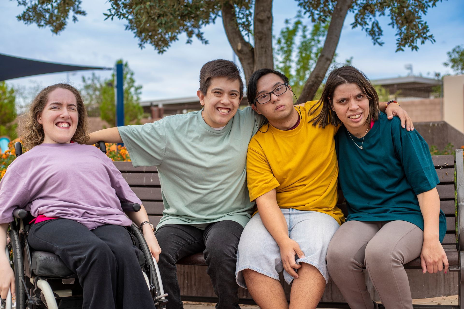 A group of people are sitting on a bench together . one of the people is in a wheelchair.