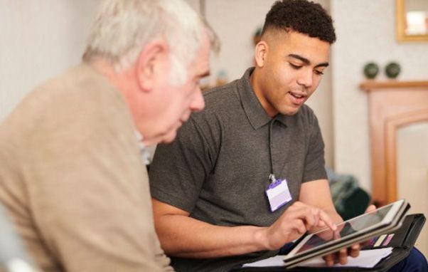 Young man with tablet showing a senior in a home setting. He is pointing at the screen.