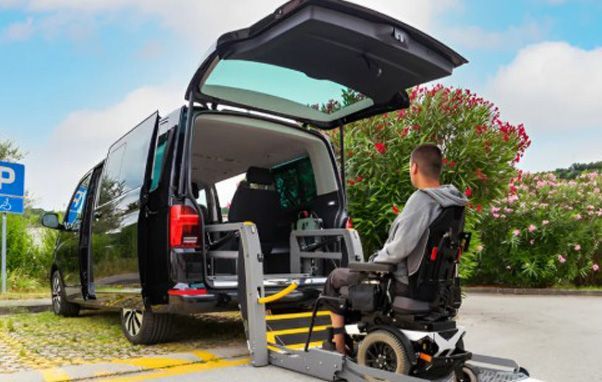 Person in wheelchair using ramp to enter accessible van, parked outdoors.