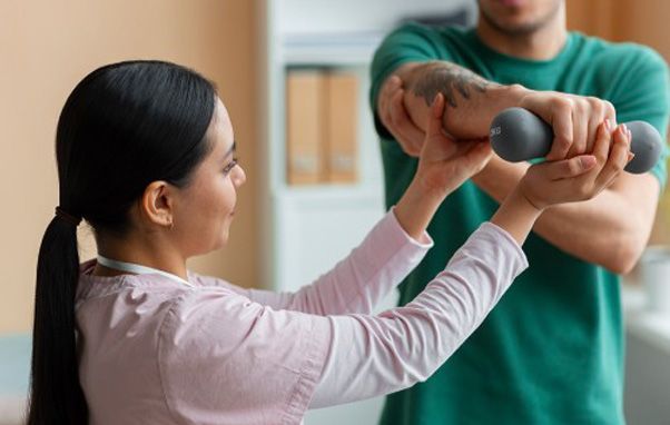Woman assisting a man with dumbbell arm exercise. Indoors, tan walls.