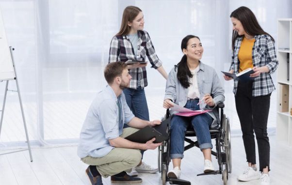 A diverse group of four people, including a woman in a wheelchair, in an office, collaborating on work.