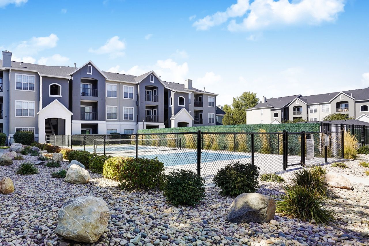 Exterior view of a multi-building apartment complex with a fenced pool and desert landscaping.