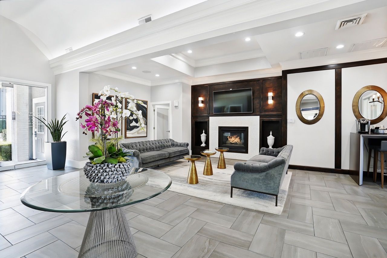 Bright modern community lounge with sofas, glass table, fireplace, and TV.