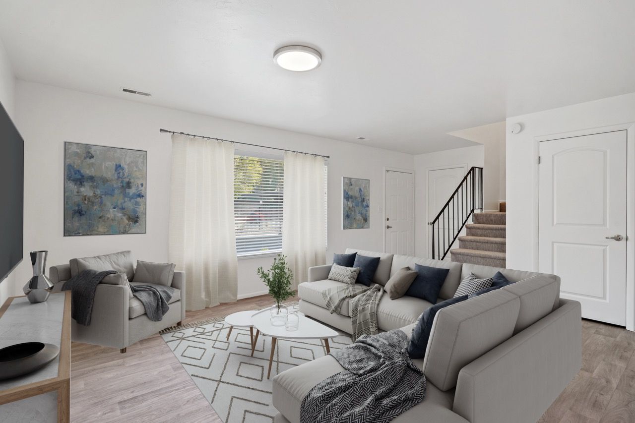 Bright living room in an apartment with a gray sectional, armchair, white curtains, and a staircase.