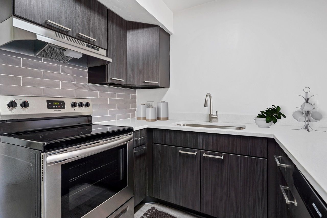 Modern kitchen with dark wood cabinets, stainless steel stove, and white countertops.