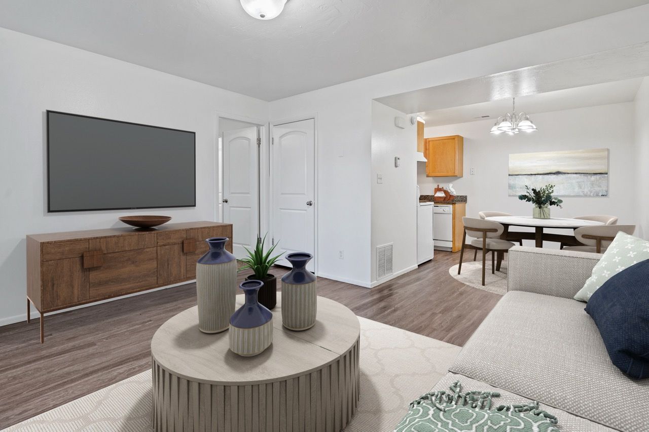 Living room with a wall-mounted TV, round coffee table, and open kitchen/dining area.