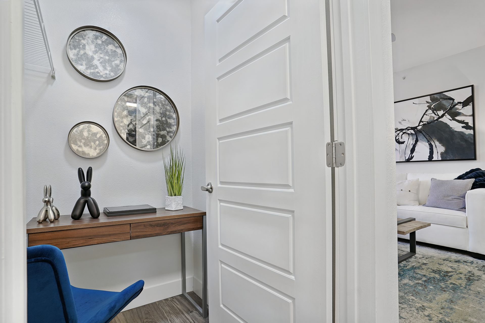 Entryway with wooden desk, three round mirrors, and a blue chair. Living room visible through the open door at Preston Hollow in Millcreek, UT.