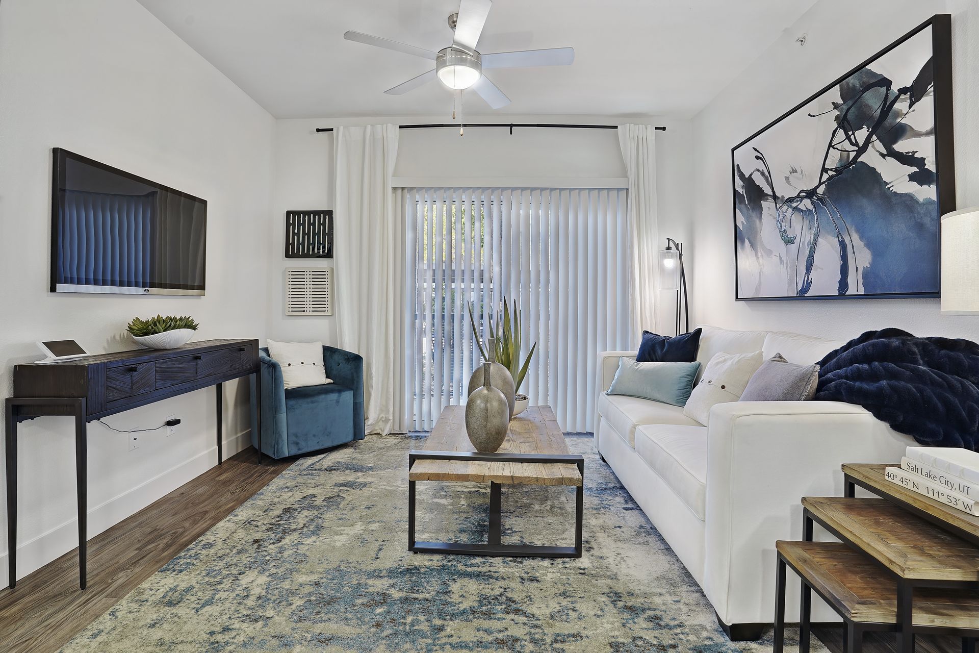 Living room with white walls, blue rug, white sofa, and a TV mounted on the wall at Preston Hollow in Millcreek, UT.