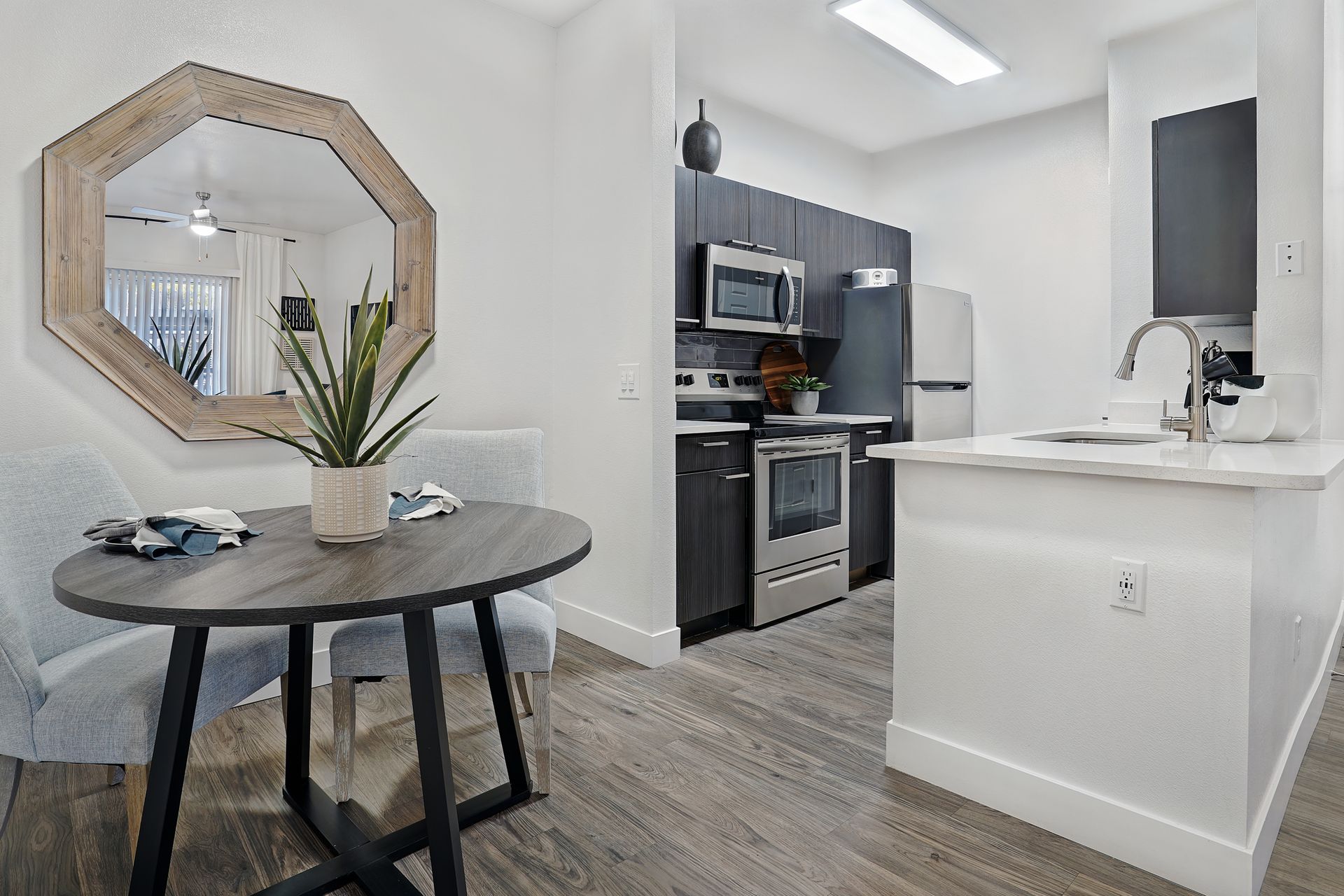 Dining area with round table, chairs, and kitchen in background. Light wood floors, white walls at Preston Hollow in Millcreek, UT.