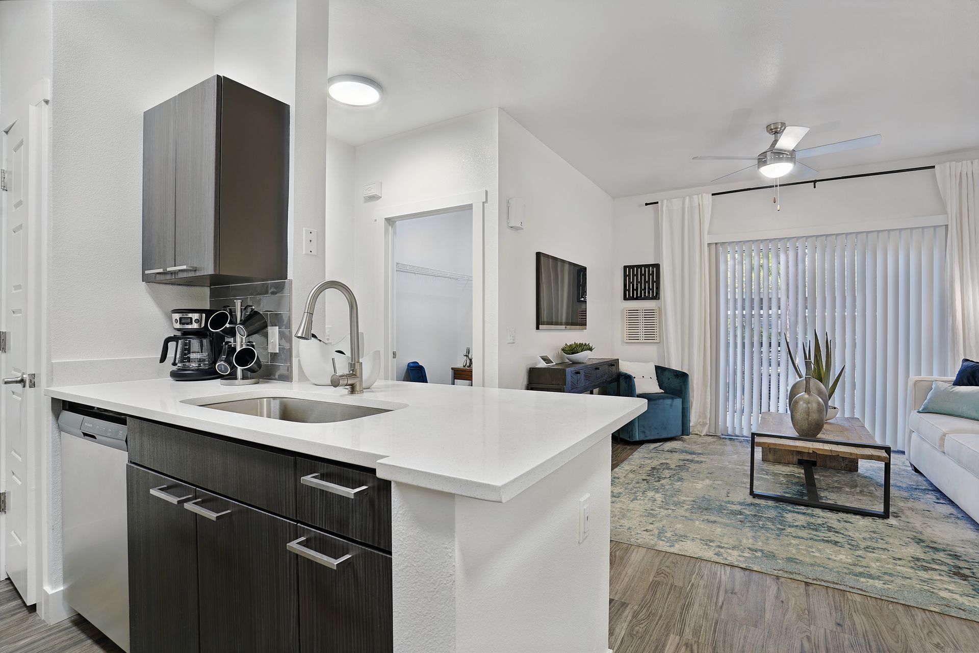 Modern kitchen with white countertops, dark cabinets, and stainless steel appliances; living room in background at Preston Hollow in Millcreek, UT.