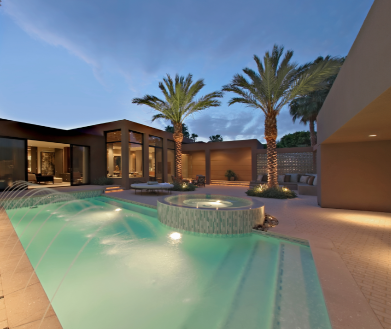A large swimming pool surrounded by palm trees in front of a house