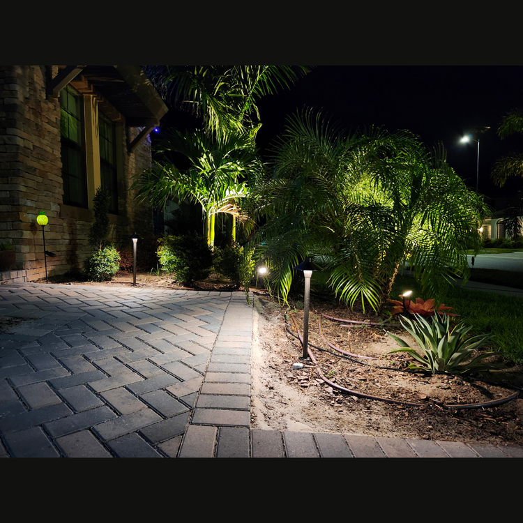 A brick walkway is lit up at night in front of a house.