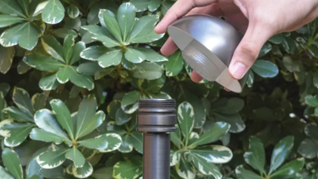 A person is holding a metal object in their hand in front of a bush.