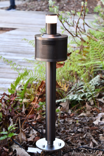 A pole with a light on it is sitting in the middle of a garden.