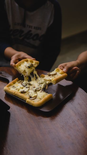 Hands pulling apart a cheesy baked pastry on a wooden table in dim light