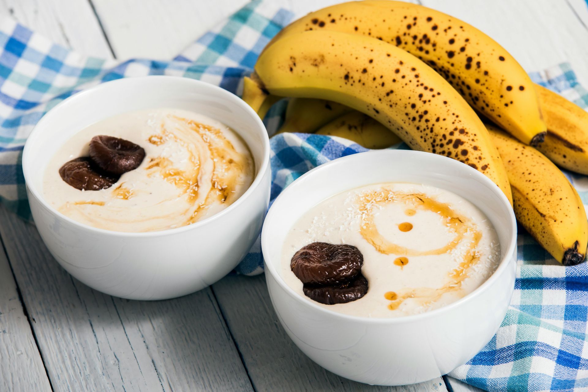 Two bowls of yogurt with bananas on a blue checkered cloth