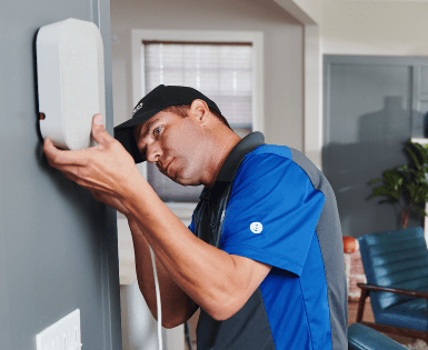 A man in a blue shirt is installing a security system on a wall.