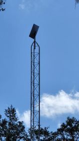 Tall metal tower with a Starlink dish a blue sky, framed by trees below